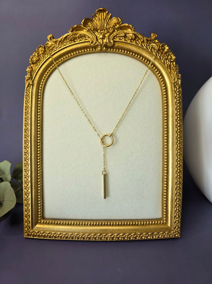 The Sleek Gold Y-Necklace Choker, a gold-plated stainless steel lariat necklace featuring a fine chain, a small circular component, and a polished vertical bar drop pendant