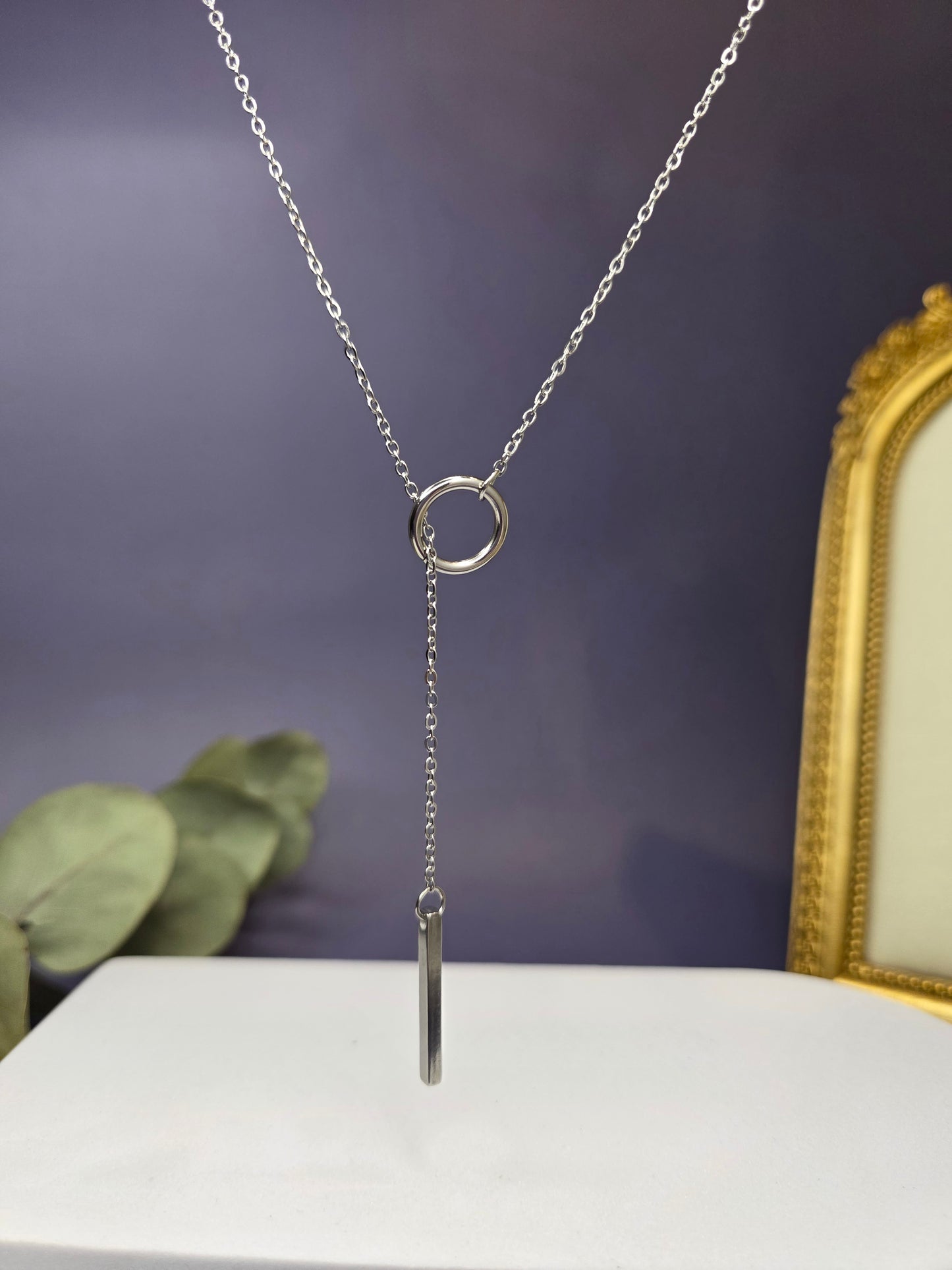 The Sleek Silver Y-Necklace Choker, a stainless-steel lariat necklace featuring a fine chain, a small circular component, and a polished vertical bar drop pendant.