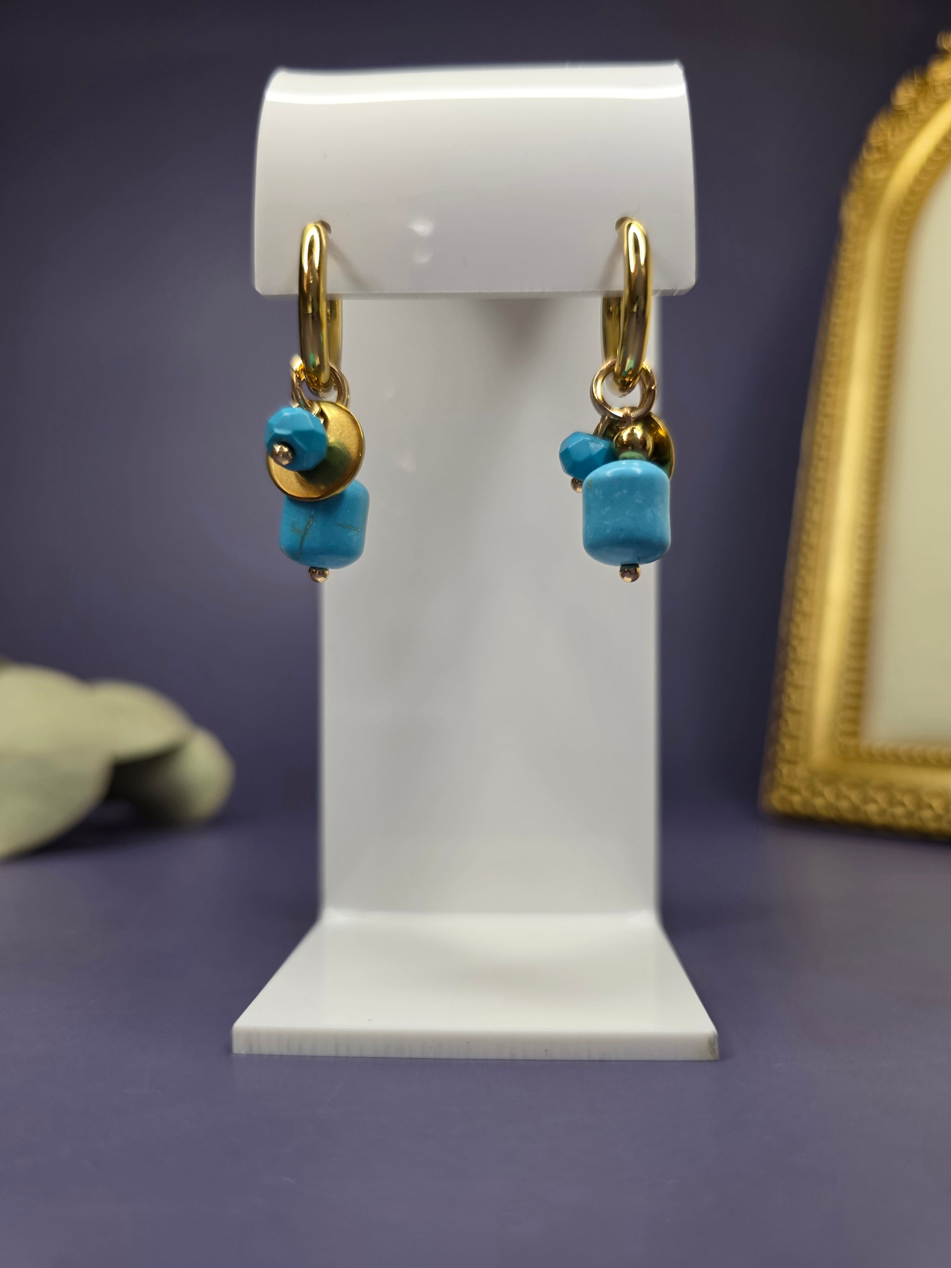 Front-facing view of the Nomad Turquoise Hoops on a white display stand. 18k gold plated huggies with turquoise stone and gold disc charms — My Silver Lining.