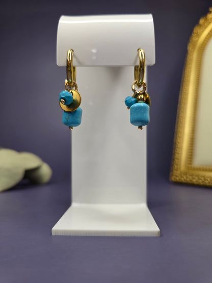 Front-facing view of the Nomad Turquoise Hoops on a white display stand. 18k gold plated huggies with turquoise stone and gold disc charms — My Silver Lining.