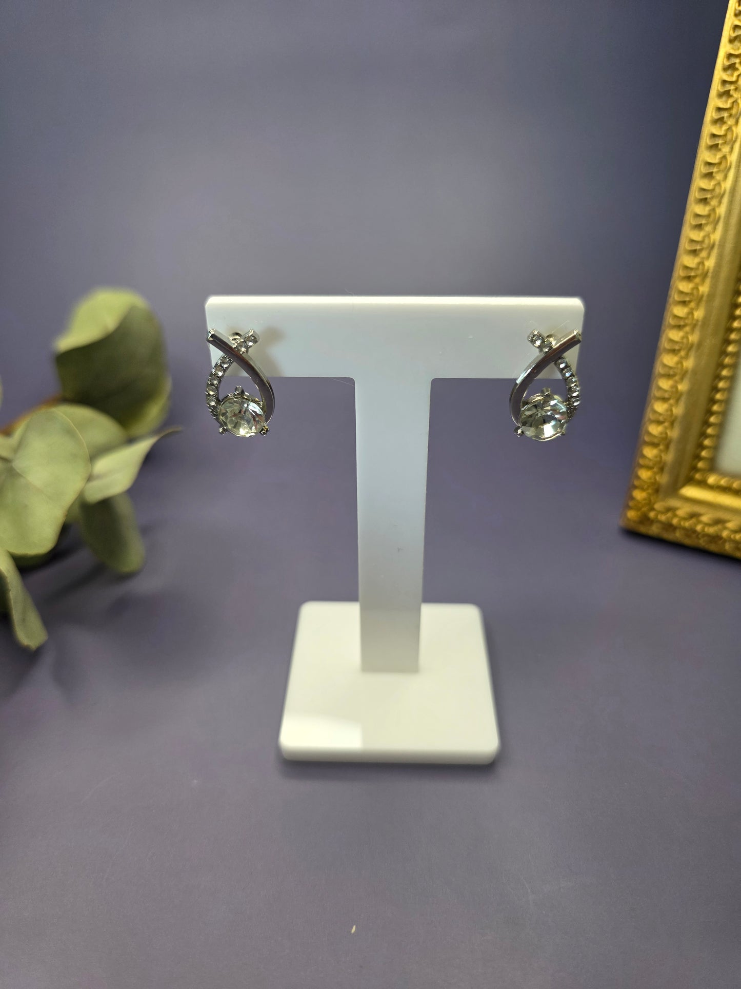 Nova Orbit earrings suspended from a white T-bar jewelry stand. These 1.8cm long silver-plated earrings showcase a unique floating stone design and shimmering rhinestone orbit - My Silver Lining.