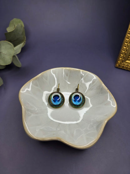 Peacock's Eye Drops displayed on a white glass bowl. These 3cm bohemian glass dome earrings feature a vibrant peacock feather design in an antique frame - My Silver Lining.