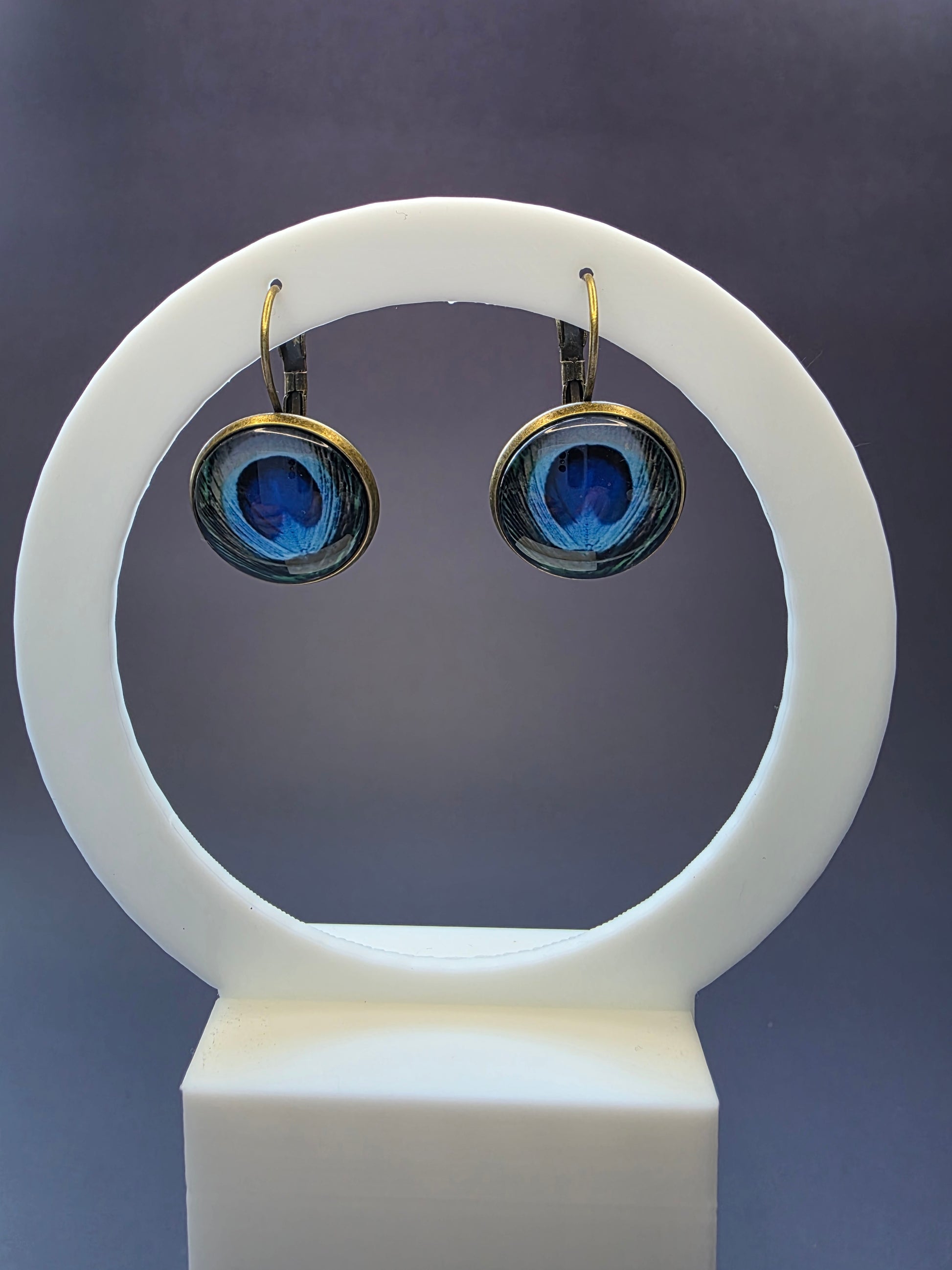 Peacock's Eye Drops featured on a white arch jewelry stand. These vintage-inspired nature earrings provide a colorful blue and green focal point with a durable alloy finish - My Silver Lining.
