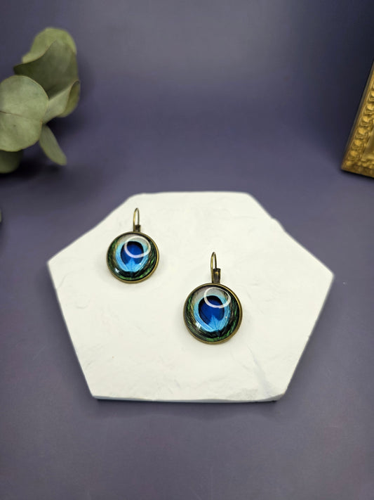 Peacock's Eye Drops displayed on a white textured hexagon stone. These 3cm bohemian glass dome earrings feature a vibrant peacock feather design in an antique frame - My Silver Lining.