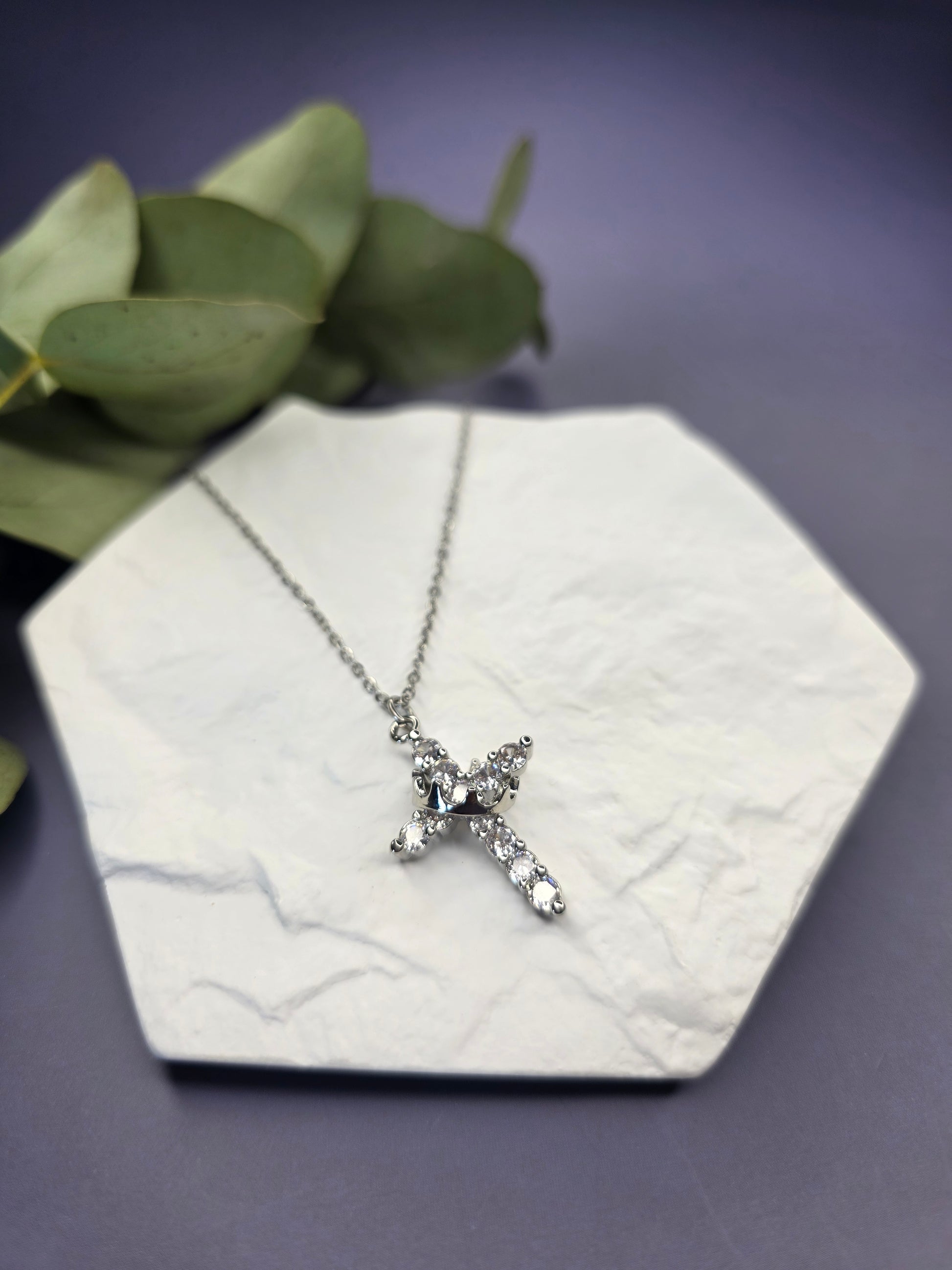 Shimmering Silver Grace necklace displayed on a white textured hexagon stone. This waterproof stainless steel cross features pave-set cubic zirconia for a brilliant, tarnish-resistant shimmer — My Silver Lining.