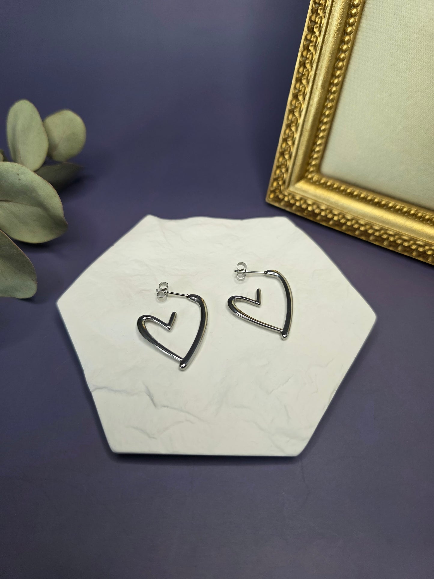 Silver open heart earrings presented in a flat lay on a white textured stone. Crafted from tarnish-resistant 316 stainless steel, these hypoallergenic heart studs are designed for durable sophistication and lasting shine - My Silver Lining.