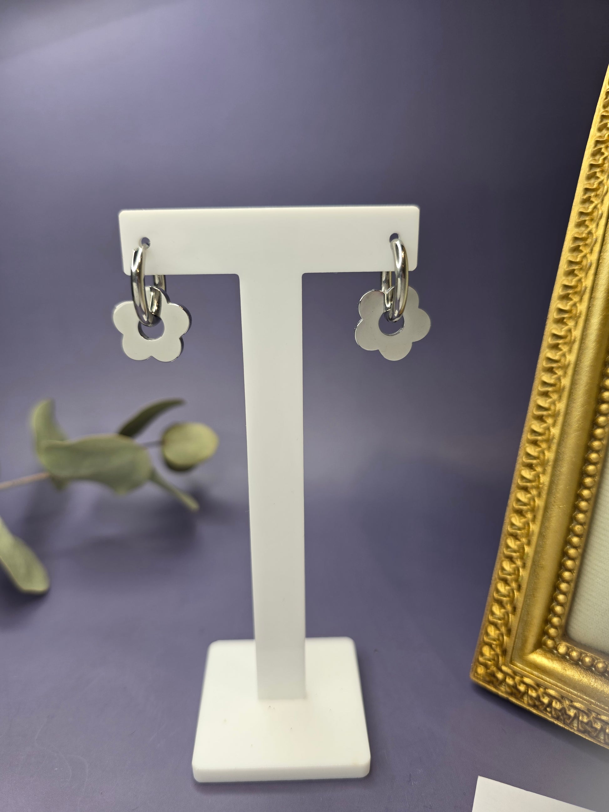 Silver Retro Bloom hoops suspended from a white T-bar jewelry stand. These high-polish silver-toned 316 stainless steel flower earrings offer a durable and chic look - My Silver Lining.