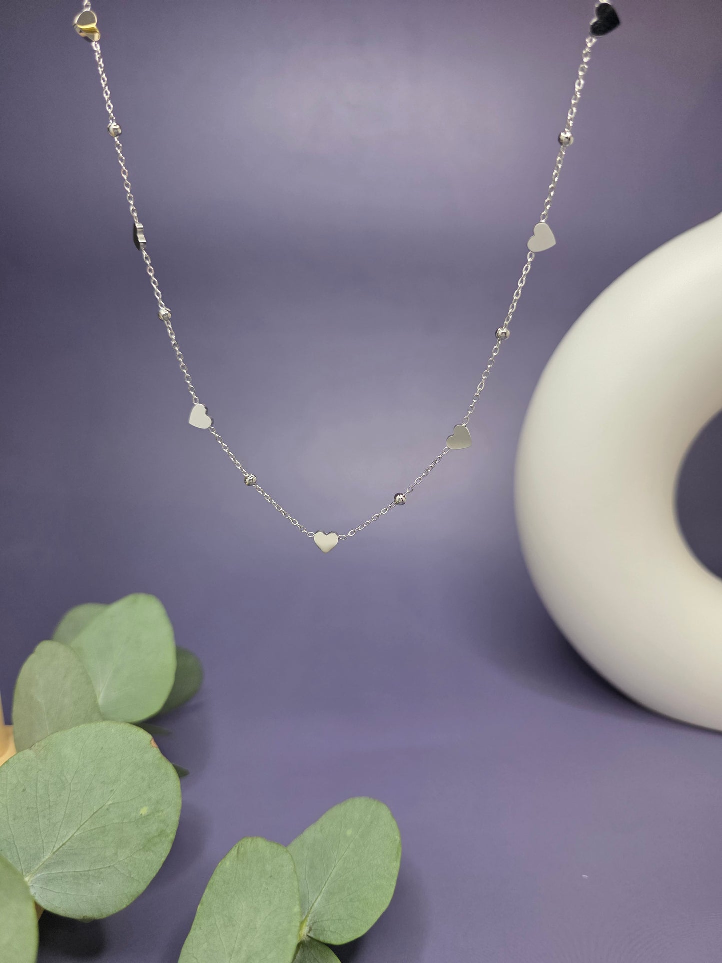 Close-up of the Silver Rhythm Heart Necklace in a floating composition against a soft purple background. This waterproof jewelry features multiple polished heart charms for a contemporary and elegant statement - My Silver Lining.