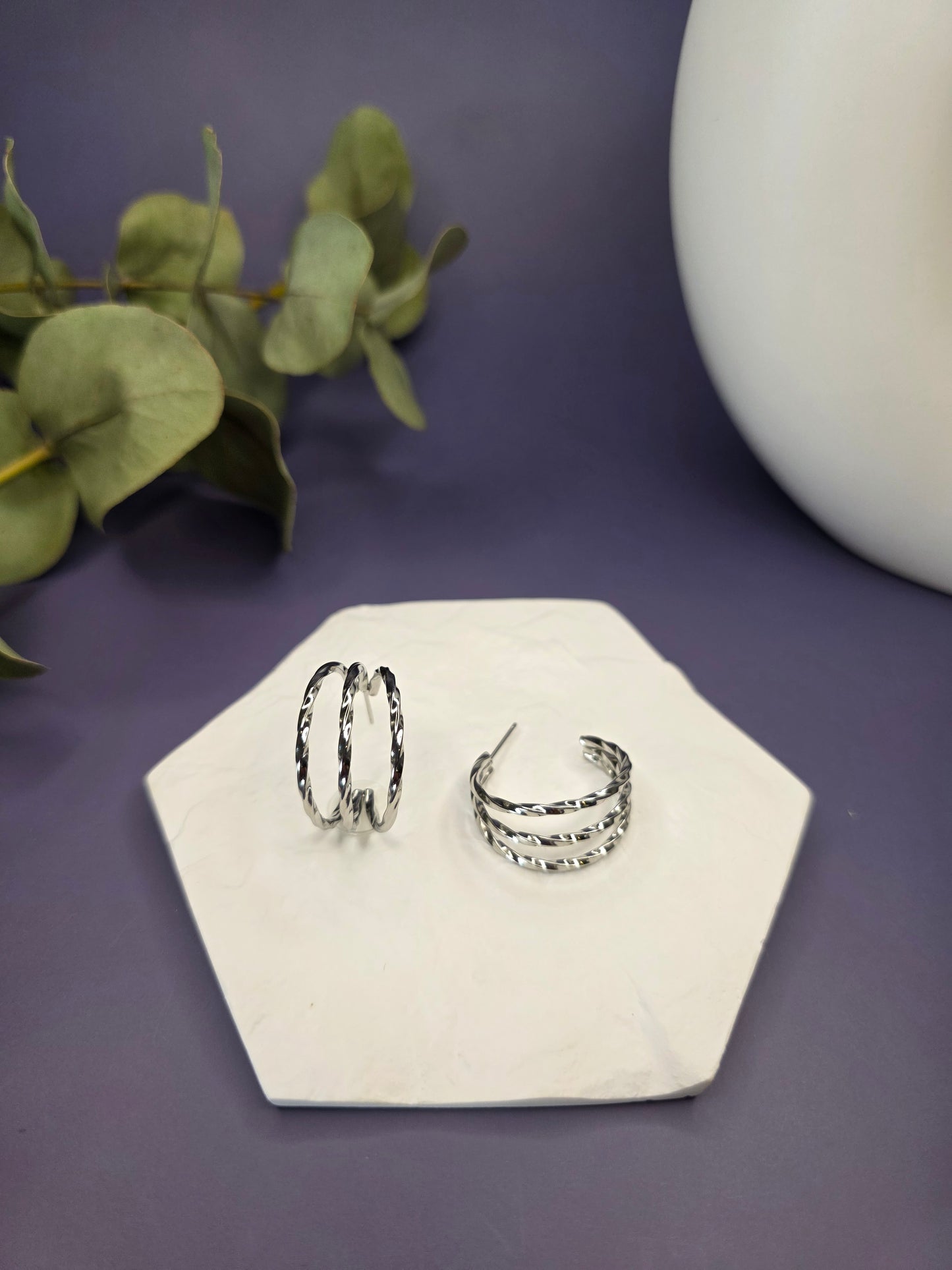 Silver Twist hoops displayed on a white textured hexagon stone. These 2.5cm triple-layered twisted earrings are made of waterproof 304 stainless steel with 316 hypoallergenic needles - My Silver Lining.