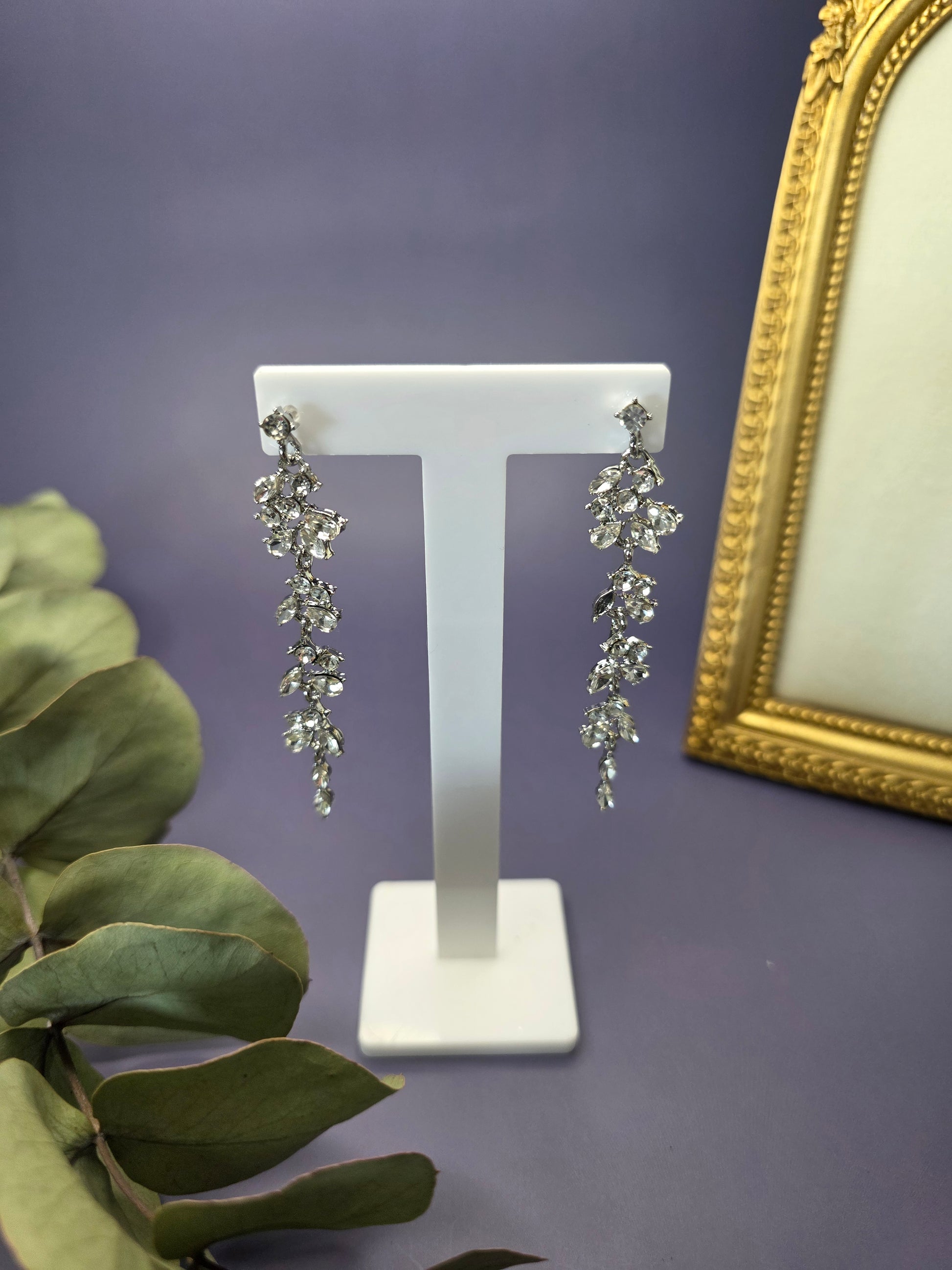 Starlight Vine Drops suspended from a golden T-bar jewelry stand. These 8cm S925 sterling silver needle earrings showcase a shimmering leaf-inspired stone cascade - My Silver Lining.