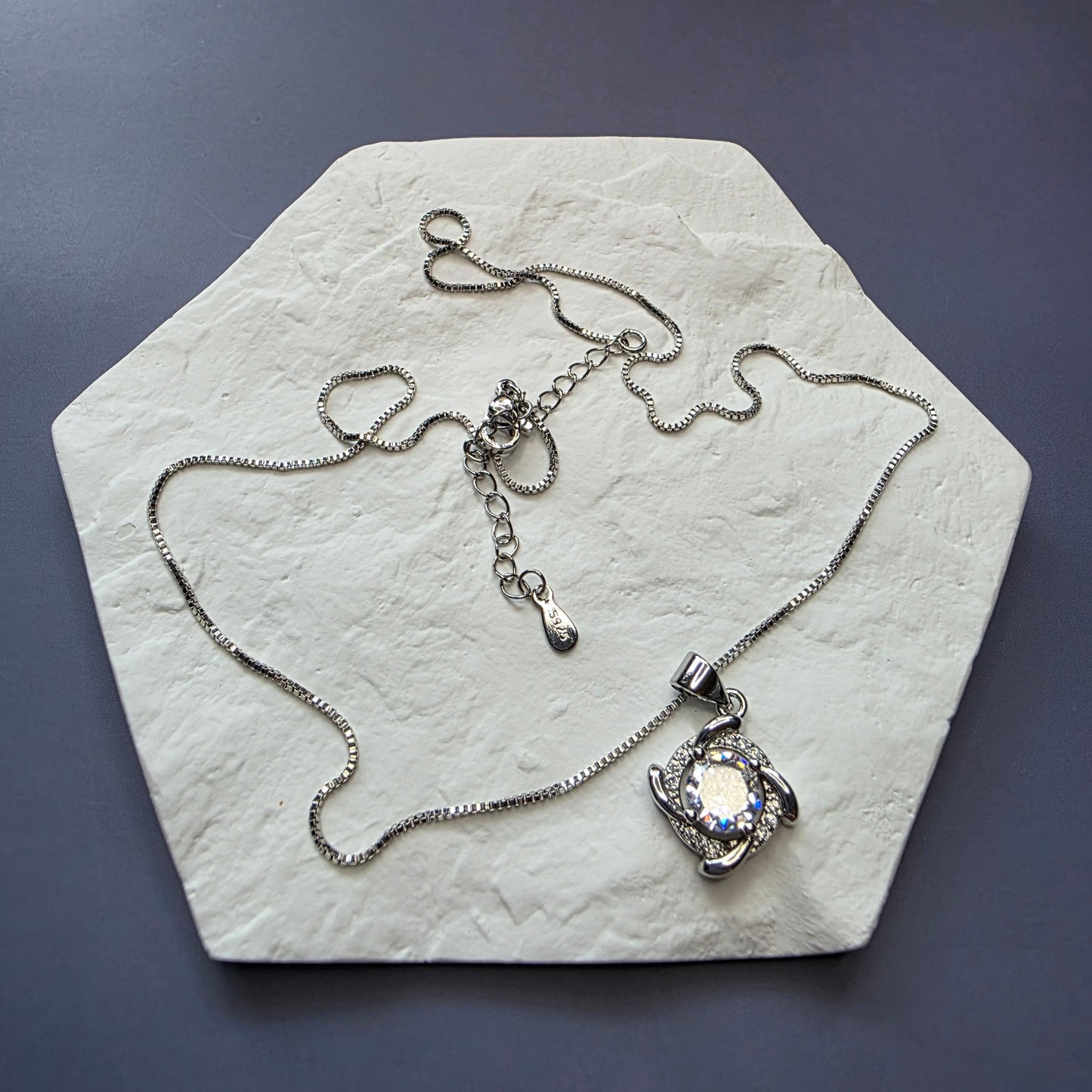 Elegant sterling silver necklace with a brilliant round cubic zirconia stone set in a polished silver swirl or halo pendant design.