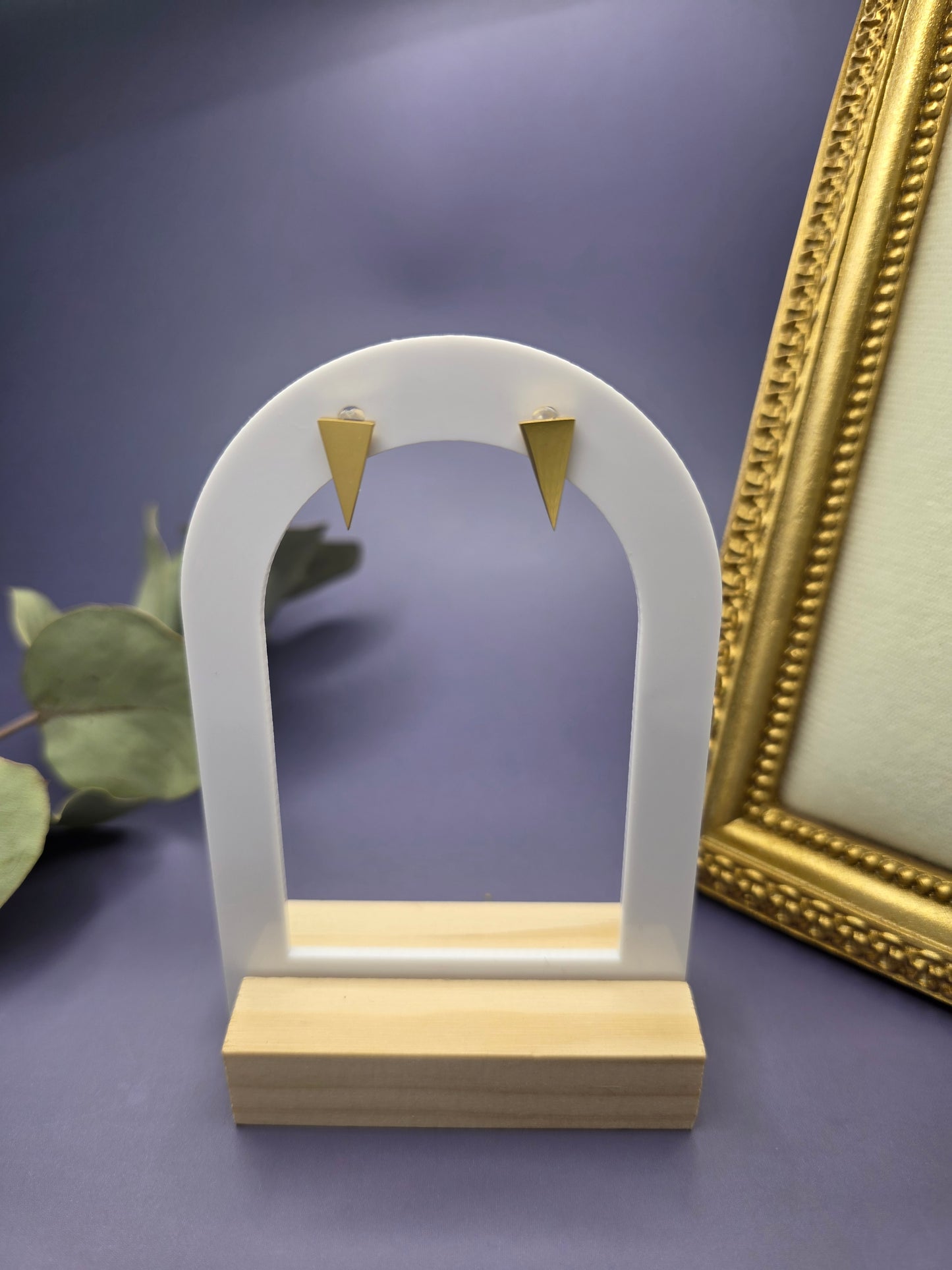 Apex Studs featured on a white arch jewelry stand. These sharp-edged triangle stainless steel studs offer a tarnish-resistant gold finish and hypoallergenic wear - My Silver Lining.