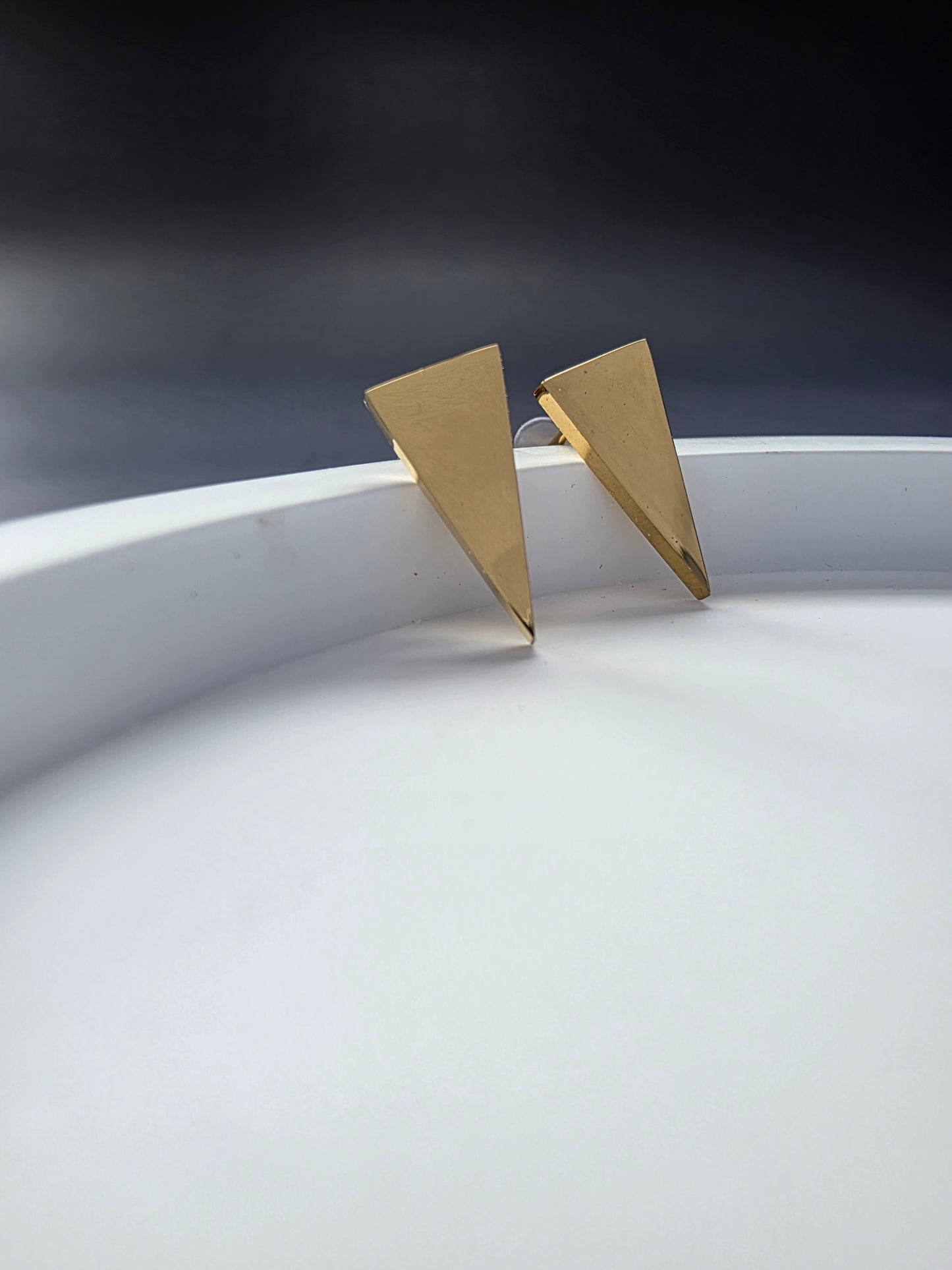 Apex Studs displayed on a white stone. These geometric triangle earrings are made of waterproof gold-toned stainless steel for a minimalist look - My Silver Lining.