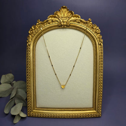 Optimized artistic shot of the gold Tiny Heart Necklace in a vintage-style frame, highlighting the polished heart detail — My Silver Lining.
