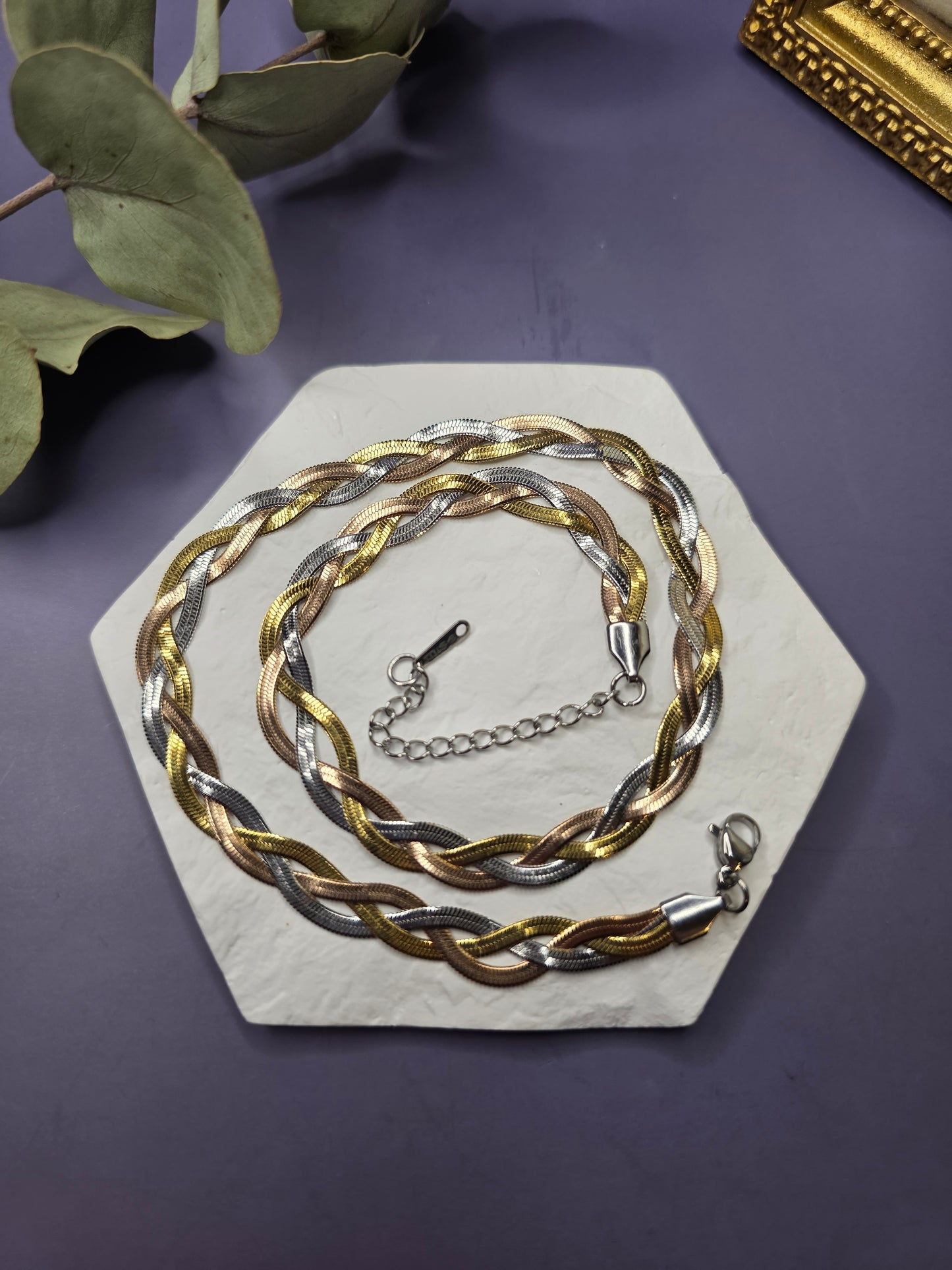 The Trinity Braid tri-tone necklace resting on a white hexagonal stone. Tarnish-resistant mixed-metal braided chain made from durable stainless steel for a versatile, contemporary look - My Silver Lining.